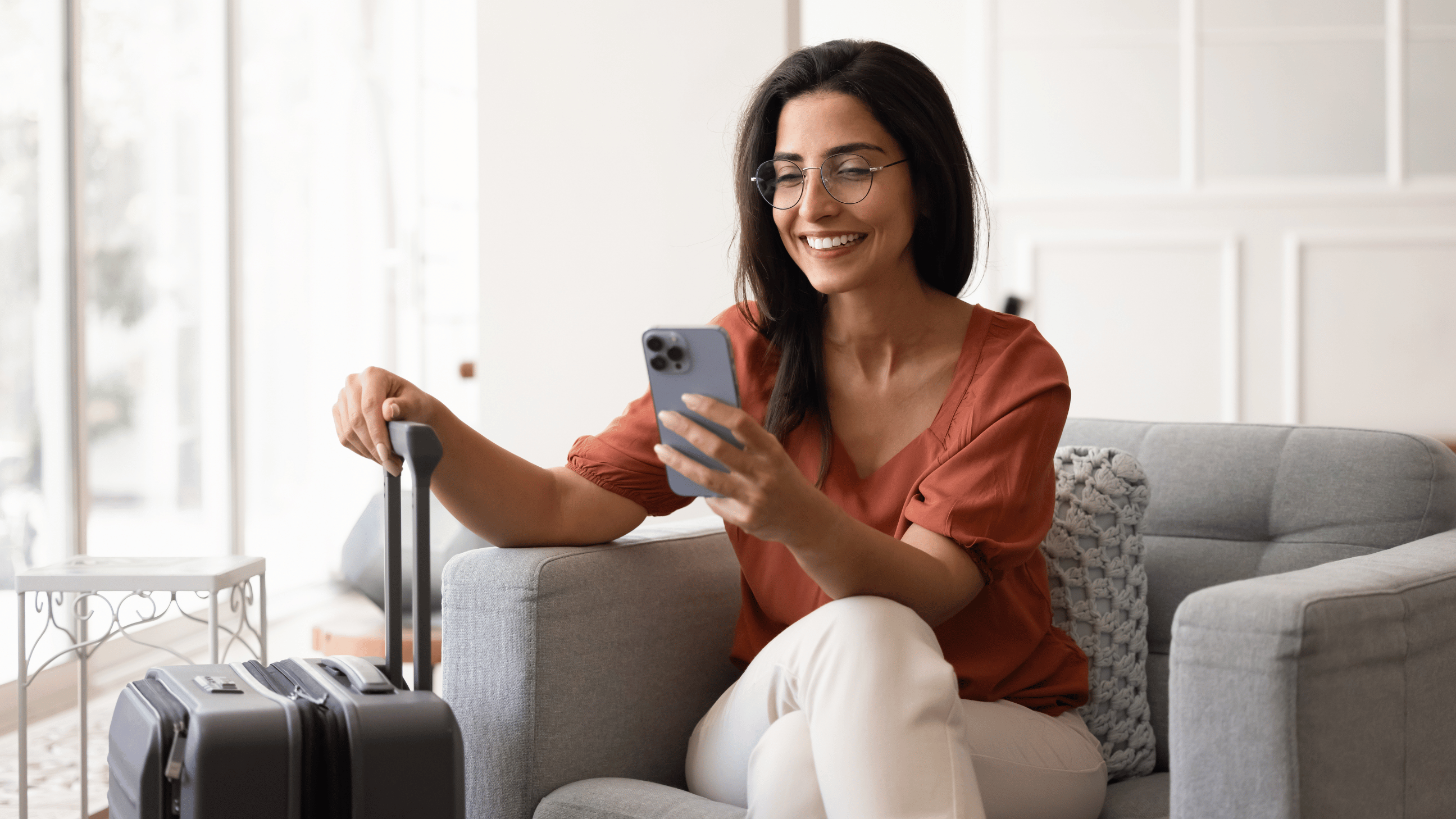 Woman sits on couch on phone & holding luggage